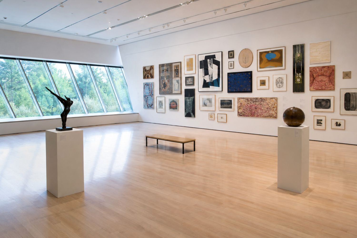 Museumzaal met sculpturen op sokkels en een wand vol ingelijste kunstwerken