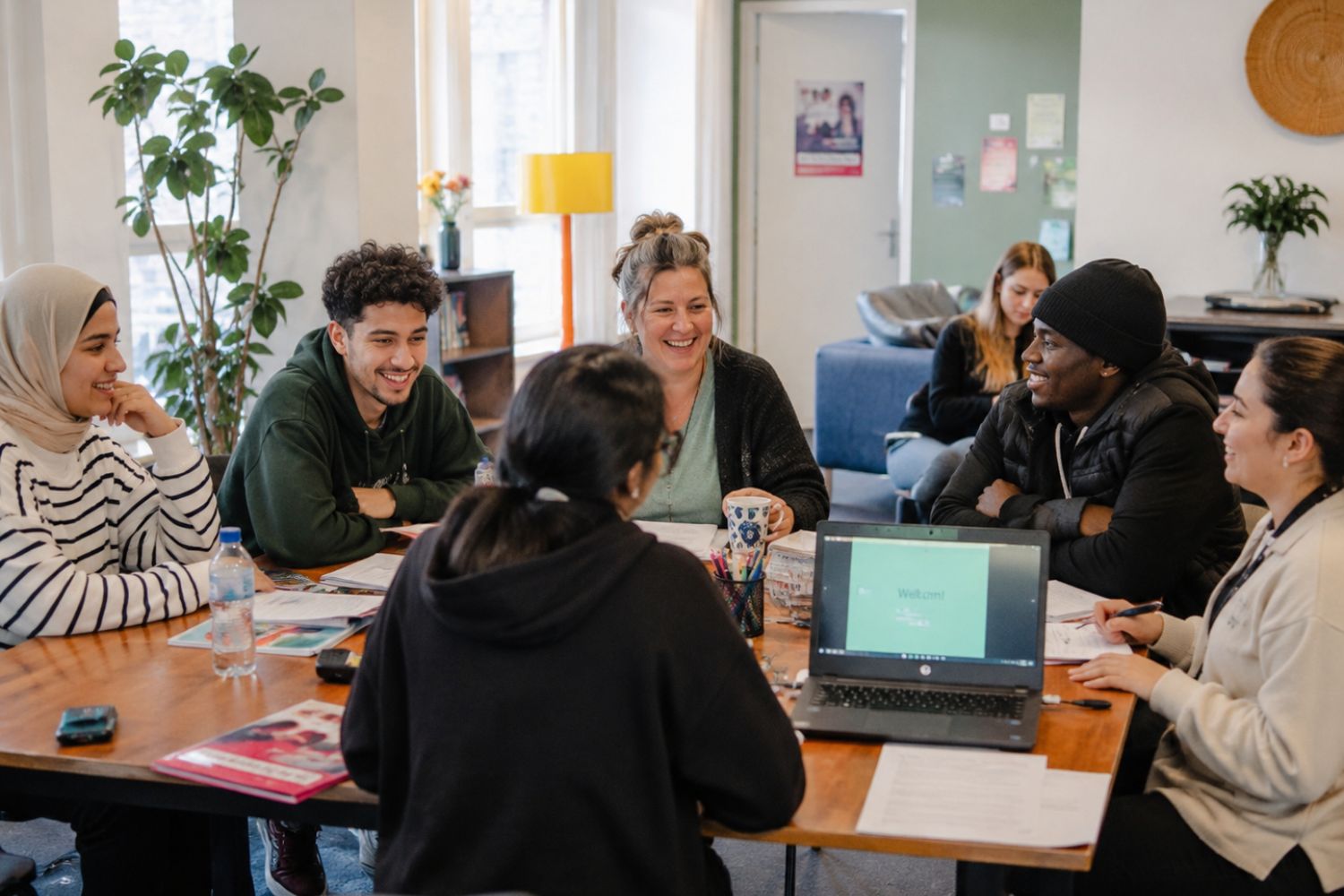 Diverse groep mensen aan tafel in een buurthuis in gesprek met een welzijnswerker